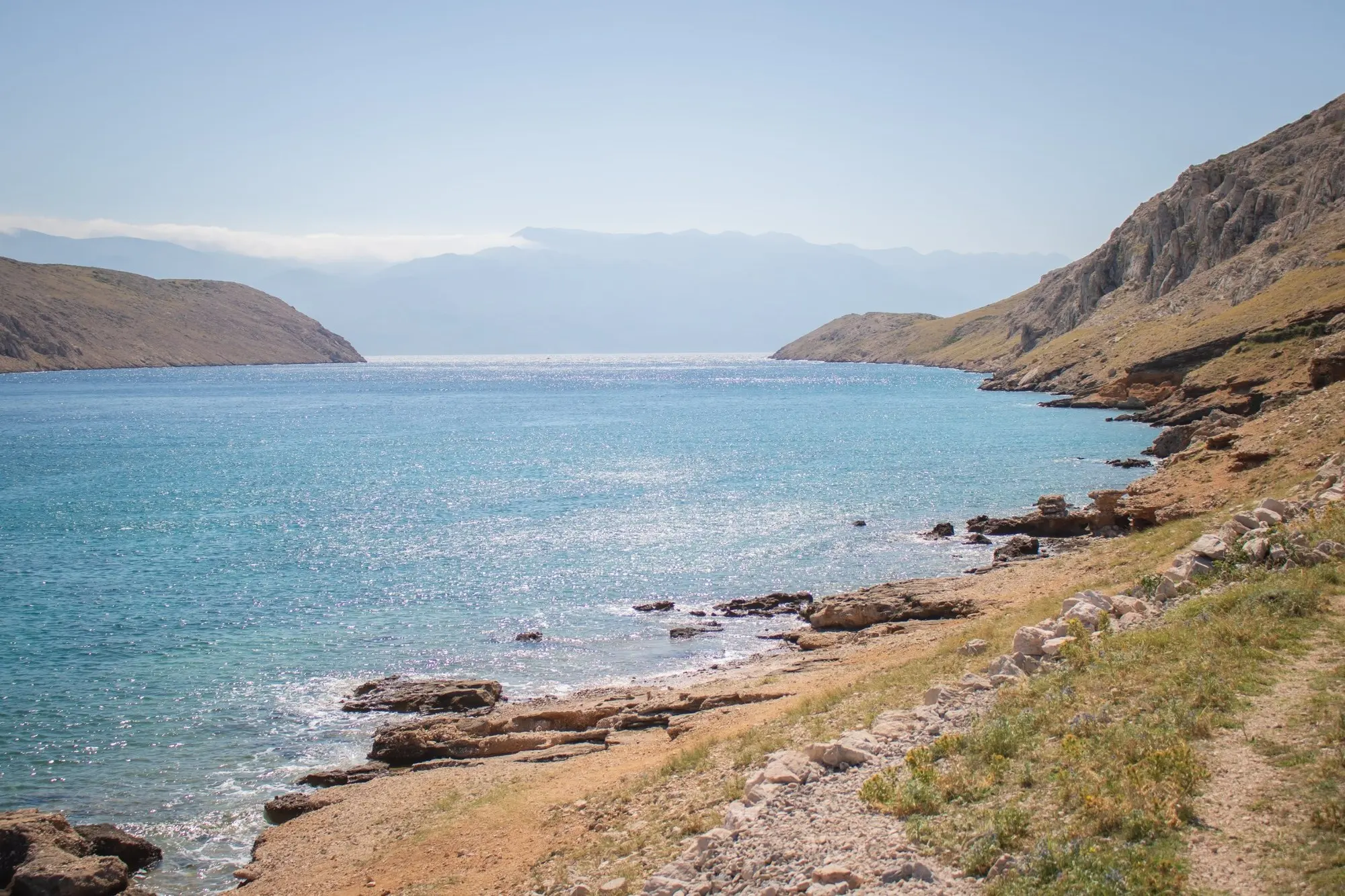 Rocky bay with glittering turquoise sea, mountains in the haze behind it