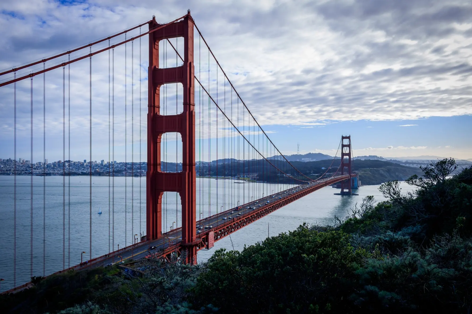 Golden Gate Bridge seen from a hill, the bay and the city behind it under clouds