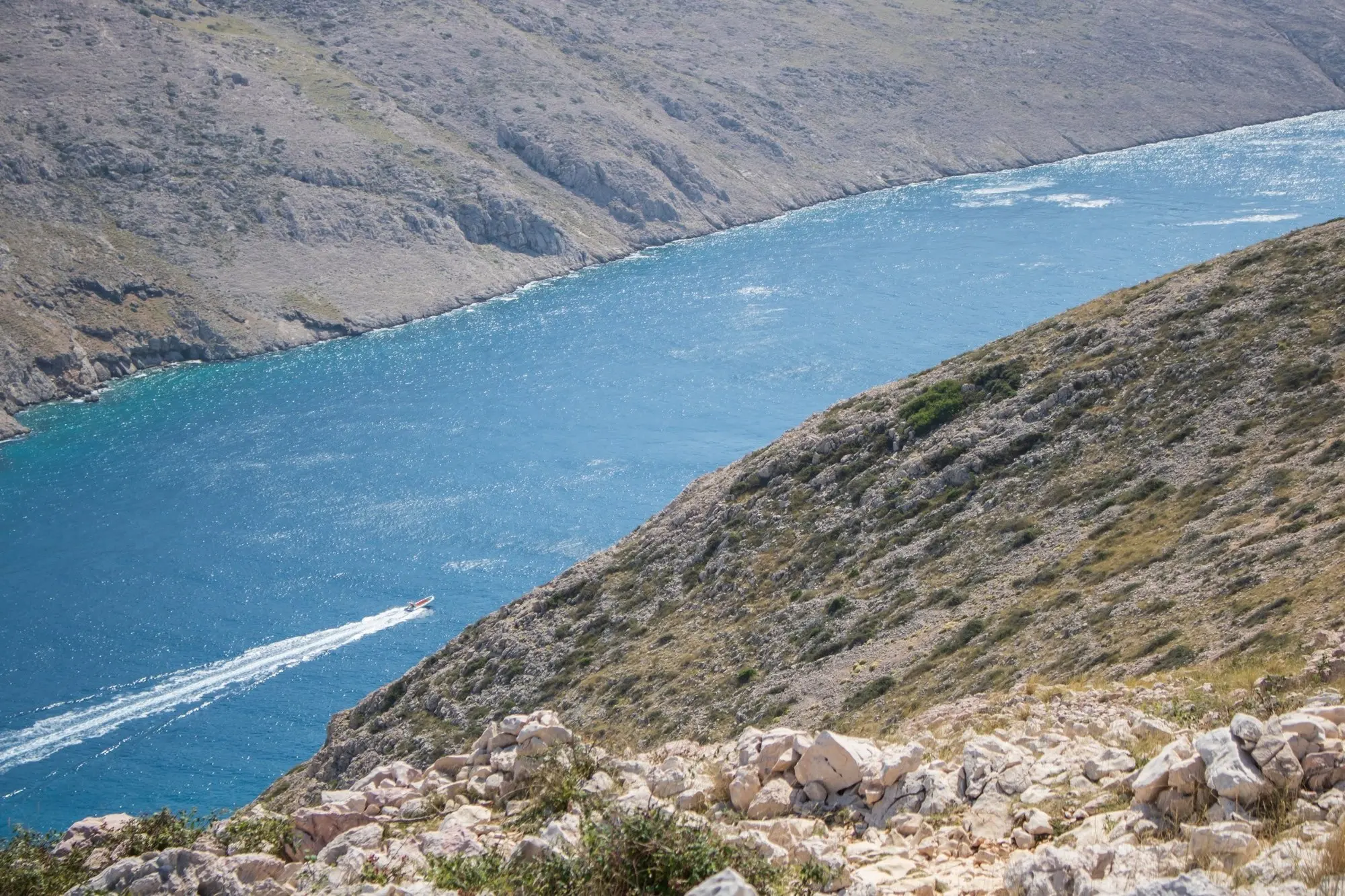 View from a stony slope onto a strait, a motorboat leaving a white wake